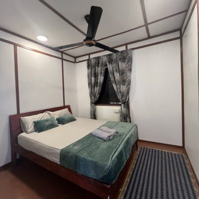 Cozy fan-cooled room with a queen-sized bed and neatly arranged green and white bedding.